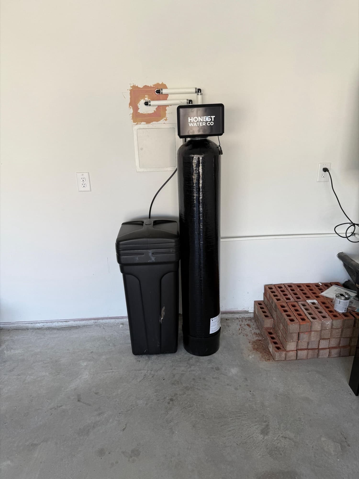 Honest Water Co softener installed in a garage with the drain line run to the wall