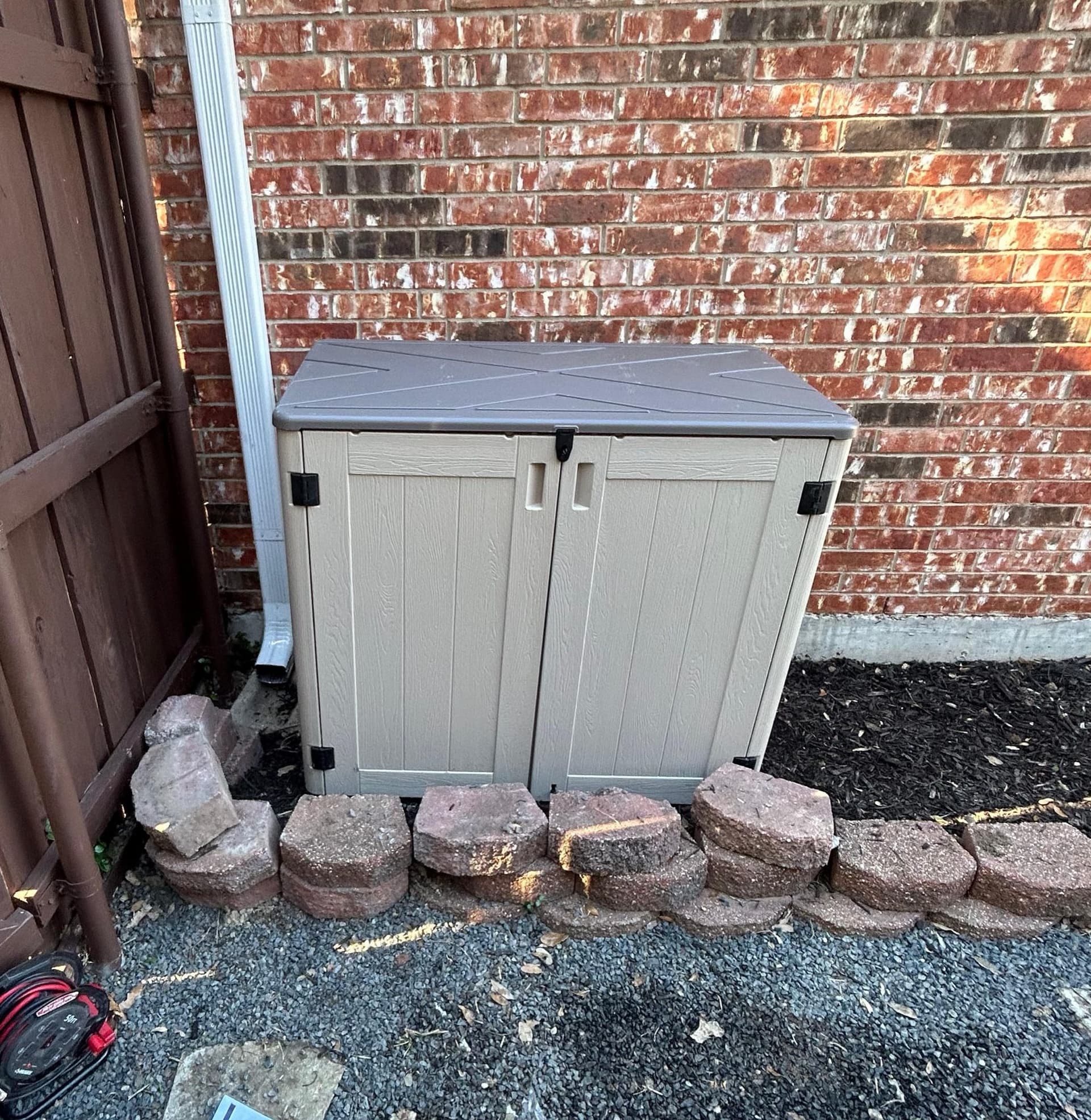 Outdoor equipment enclosure keeping a water treatment system tidy against a Texas brick home